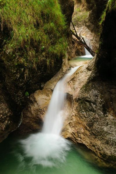 Kleiner Wasserfall fließt durch steinige Schlucht in der Almbachklamm.